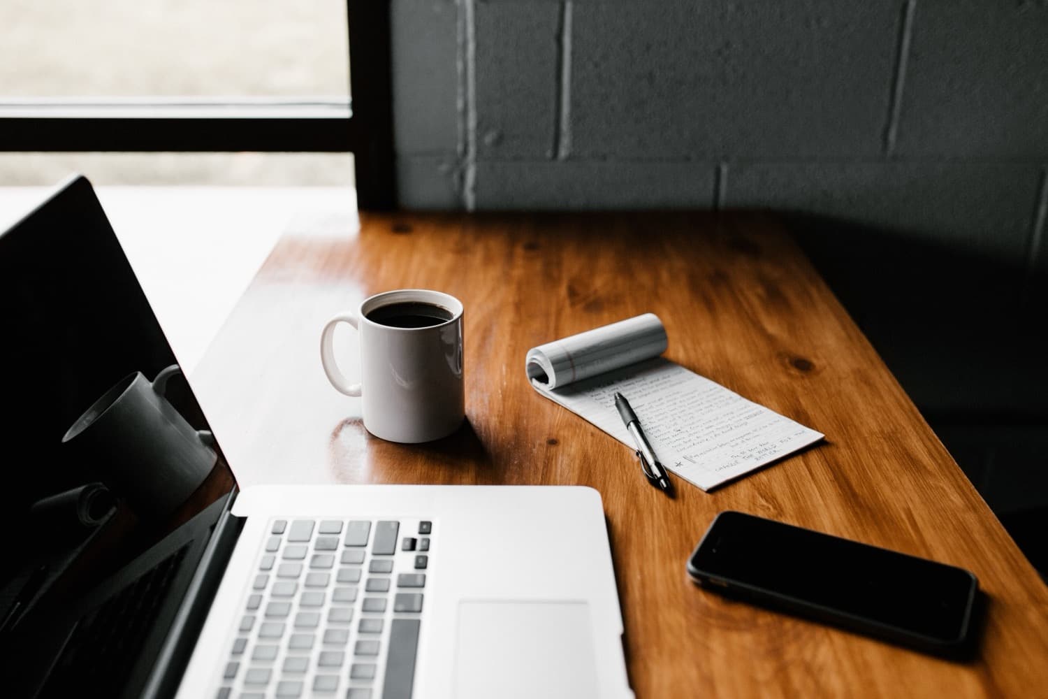 Arbeitsplatz mit Laptop, Notizbuch und Kaffee – bereit für Ihre Anfrage.